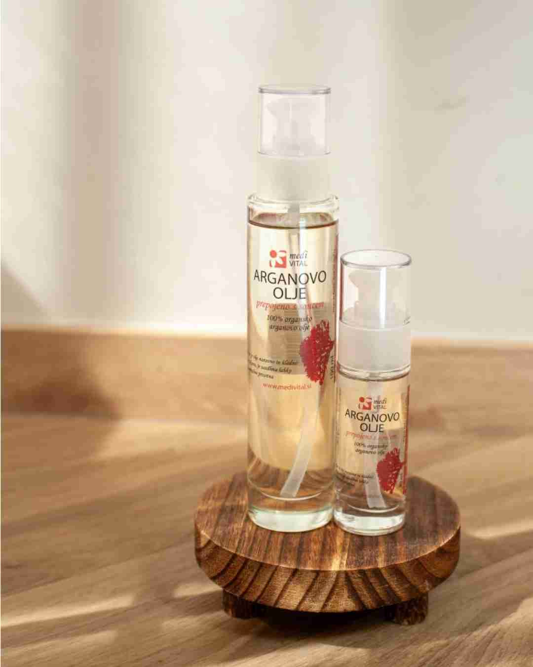 Dve steklenički arganovega olja z označeno blagovno znamko, postavljeni na leseno površino v mehki naravni svetlobi – simbolizirata naravno nego kože in las z dragocenimi rastlinskimi olji.