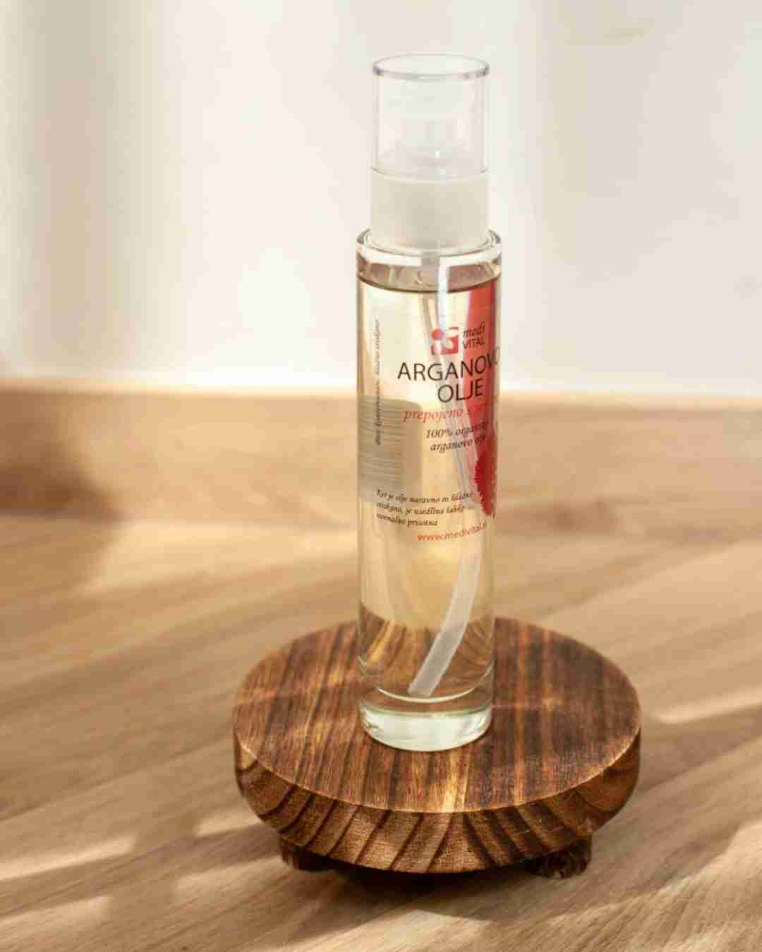 Zgornji del stekleničke z arganovim oljem s pršilko, postavljene na svetli podlagi – prikazuje praktično embalažo za nego razpokane in suhe kože na petah.
