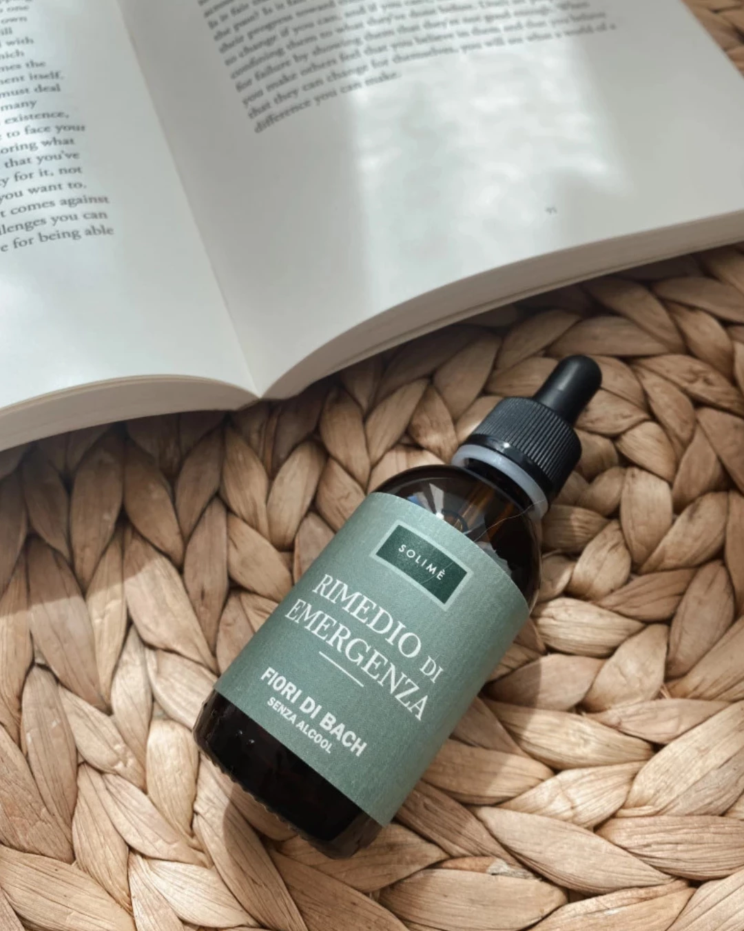 Rjava steklenička s kapalko na leseni podlagi, obdana s cvetlicami in naravnim ozadjem.