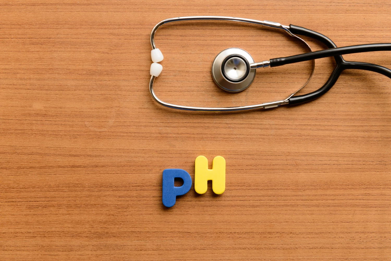Barvni črki 'pH' na leseni površini s stetoskopom – simbol ravnovesja pH vrednosti in zdravja.