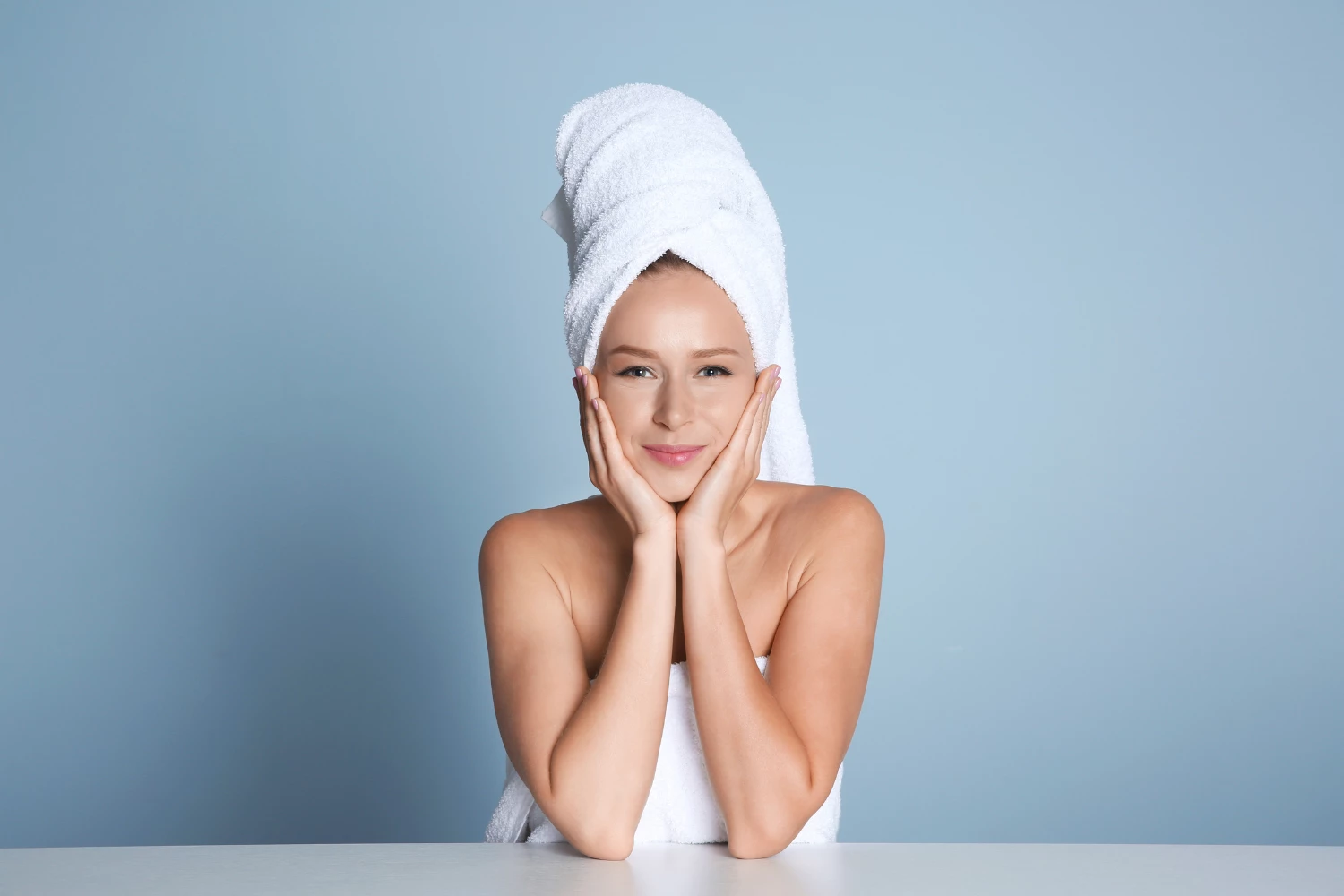 Nasmejana ženska z brisačo na glavi po negi obraza – simbol zdrave in sijoče kože.