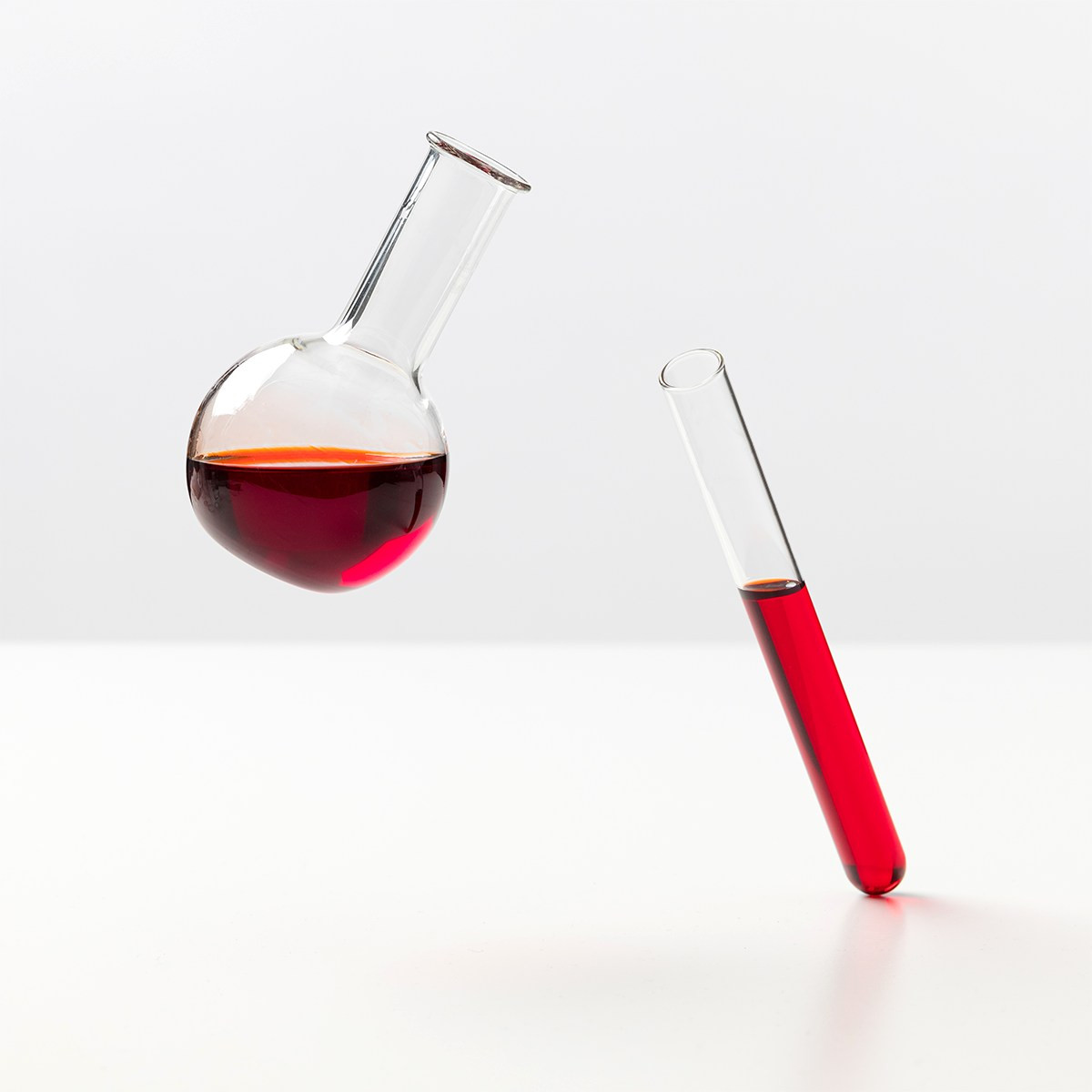 Laboratorijski bučka in epruveta, napolnjeni z rdečo tekočino, na svetli podlagi – simbolizirata znanstveno raziskovanje močnih antioksidantov, kot je astaksantin, za podporo zdravju celic in tkiv.